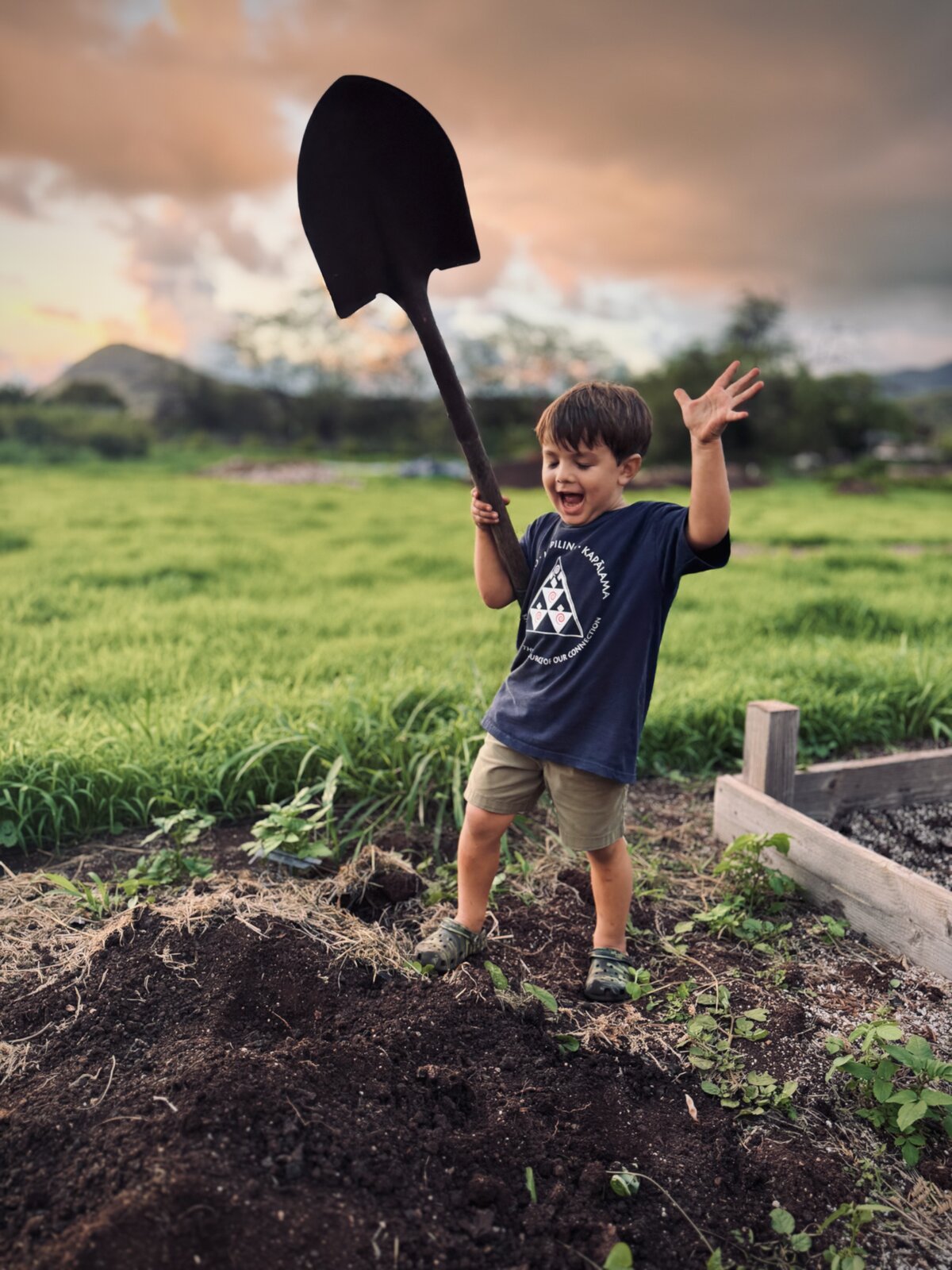 Hawaiian keiki gathered around a tray of rich soil, hands in the dirt, learning the practice of mālama ʻāina