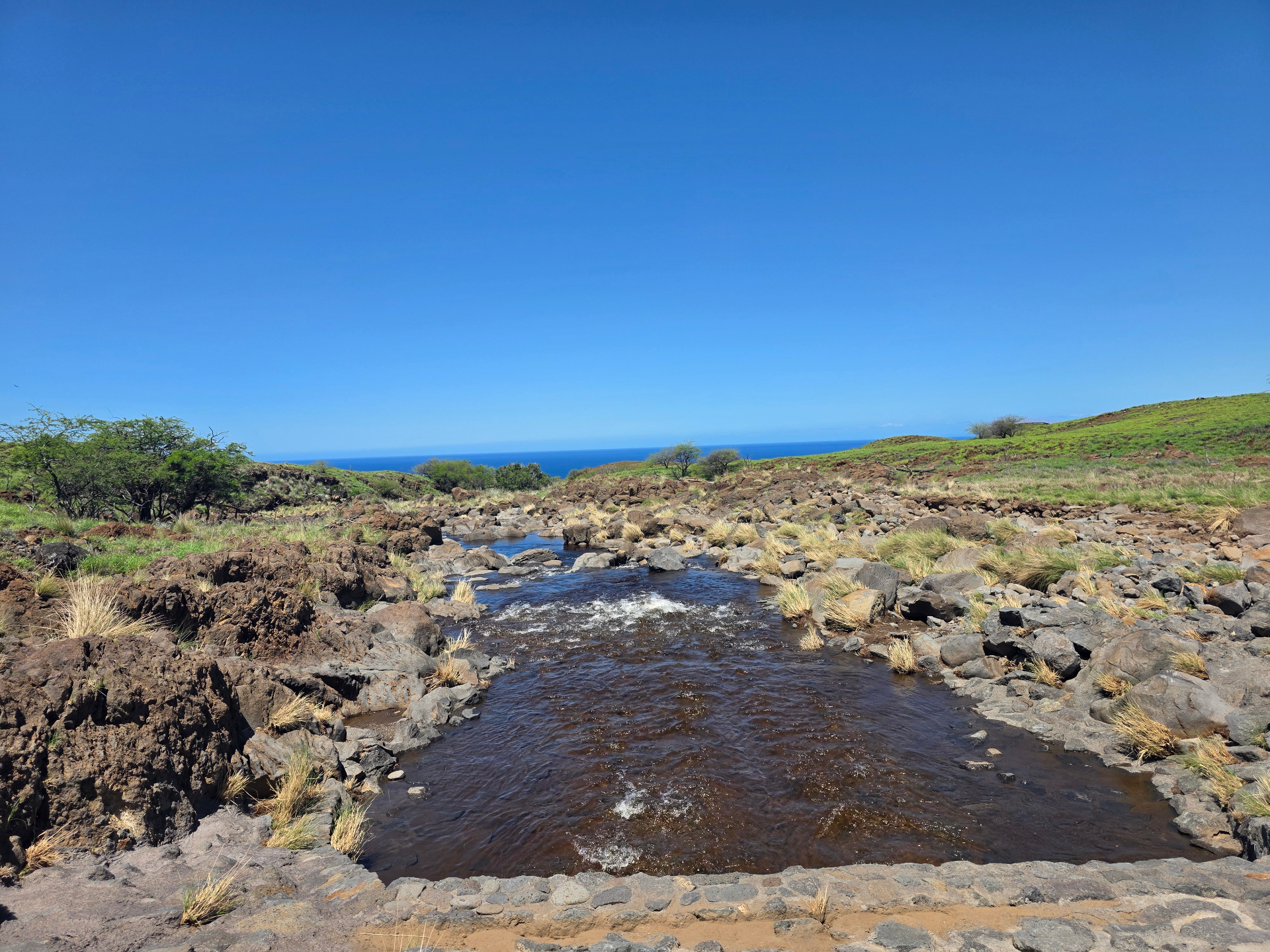 Stream flowing across lava rock toward the open ocean on the leeward Hawaiʻi Island coast